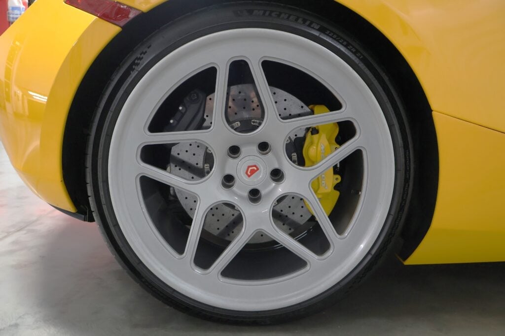 Close-up of a yellow sports car wheel with silver alloy rim, black tire, and yellow brake calipers visible through the spokes