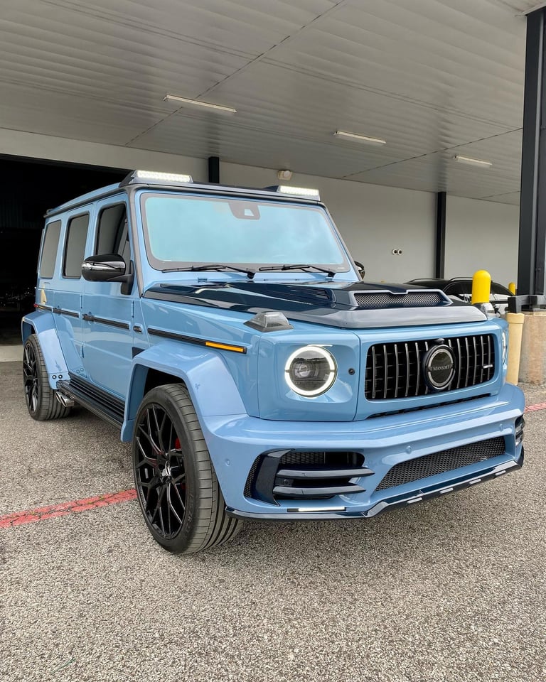Light blue Mercedes-AMG G-Class SUV parked in a garage showroom with yellow bollard visible