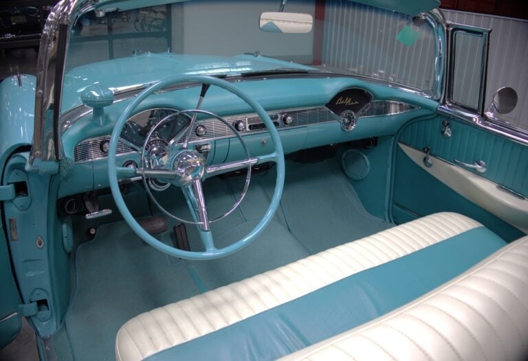 Interior of a turquoise vintage convertible car with white and teal upholstered seats, steering wheel, and dashboard visible from above
