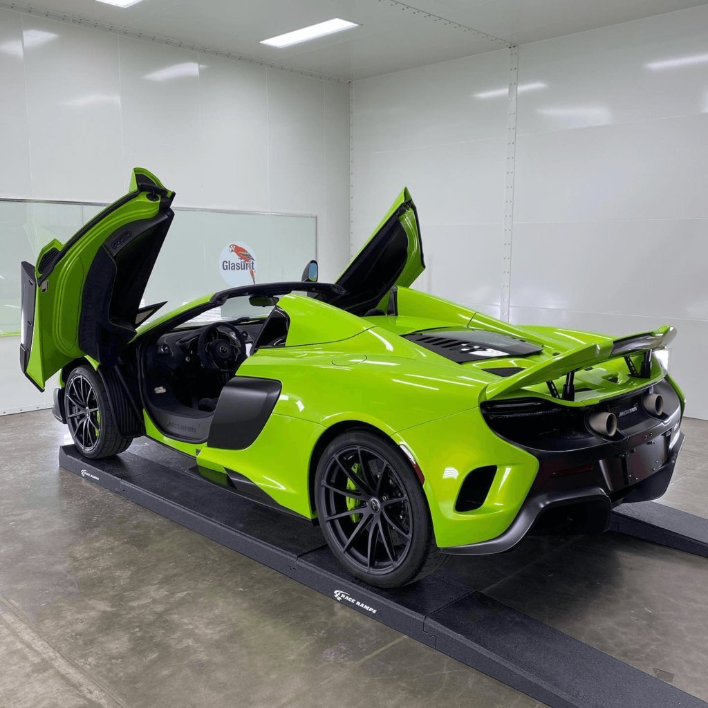 Bright lime green sports car with open gull-wing doors in a white showroom with concrete flooring