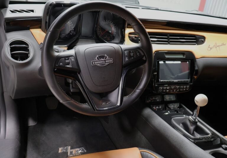 Car interior dashboard with black steering wheel, instrument cluster, touchscreen display, and manual transmission shift knob