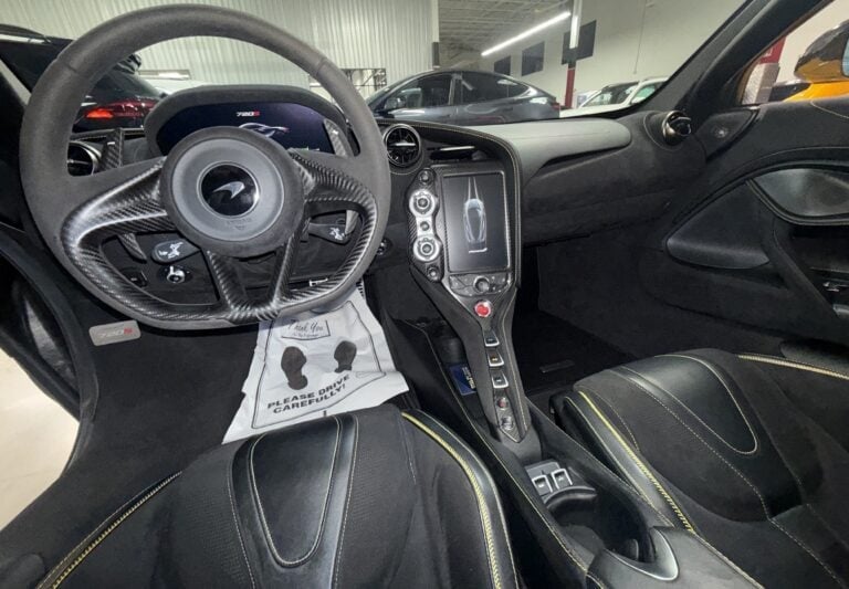 Interior of a modern sports car showing steering wheel, dashboard, center console, and black leather seats in a showroom