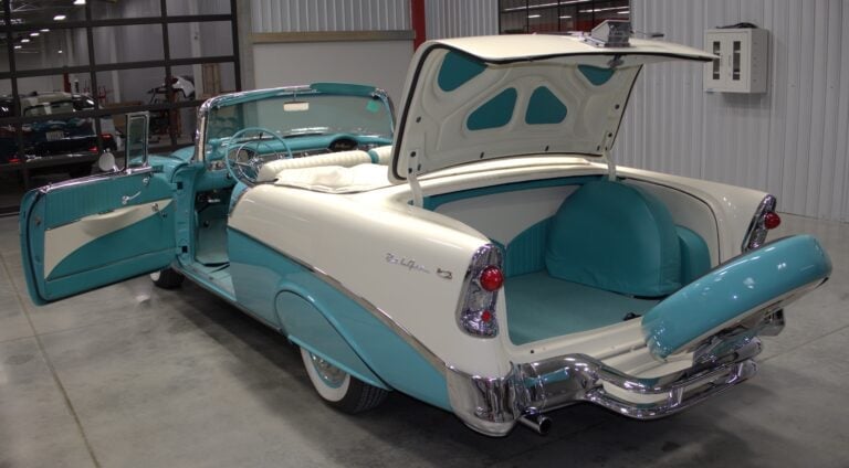 1950s turquoise and white convertible with hood and trunk open in a garage showroom, displaying its interior and classic chrome details