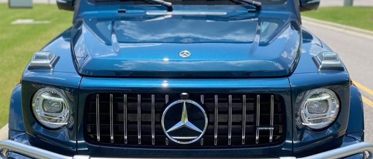 Front view of a blue Mercedes-AMG G-Class SUV with hood open, displaying grille and dual headlights