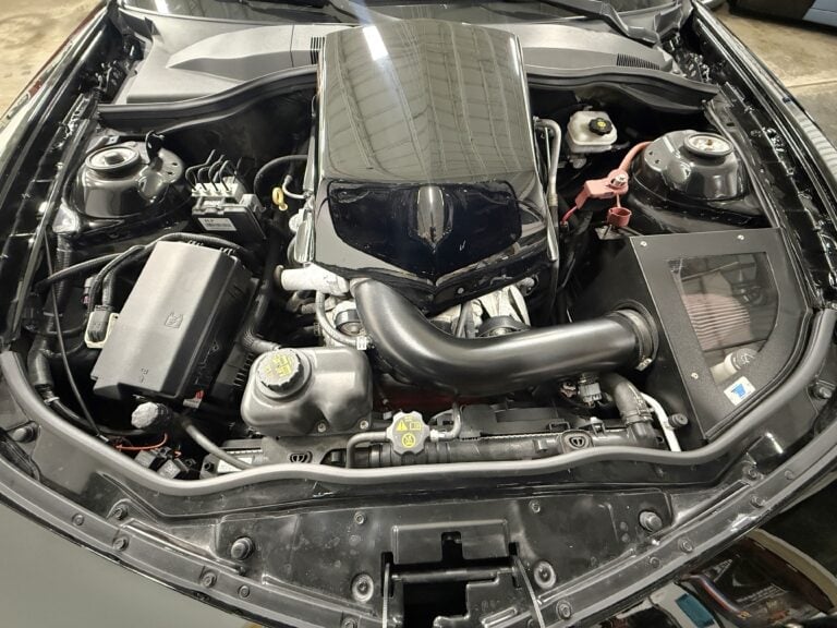 Open car engine bay showing engine block, intake manifold, hoses, and various automotive components
