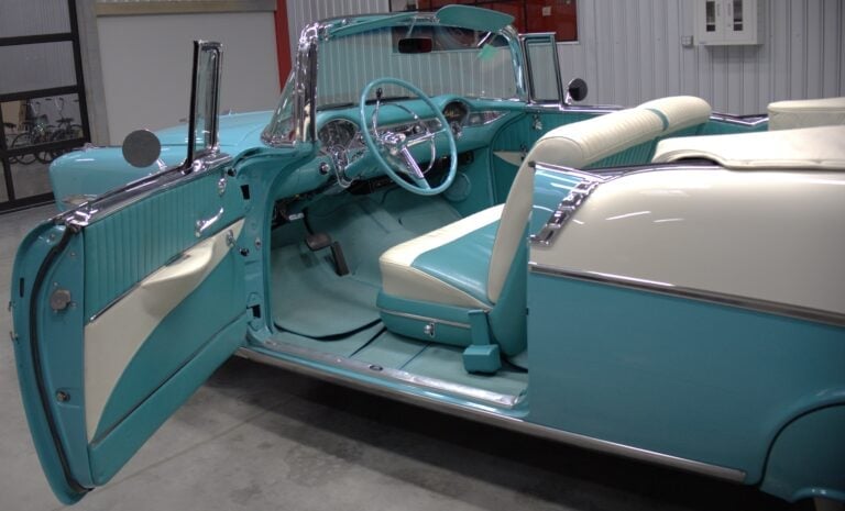 Vintage turquoise and white convertible car with open driver door showing interior steering wheel and seating in garage
