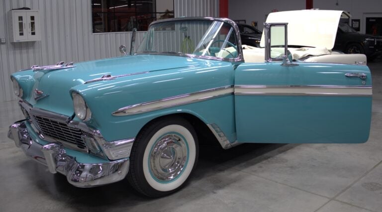 Turquoise 1956 Chevrolet convertible with white wall tires and chrome details, displayed in a garage with driver door open