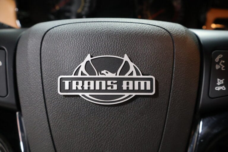 Close-up of a Trans Am steering wheel center airbag cover with white logo and text on dark leather