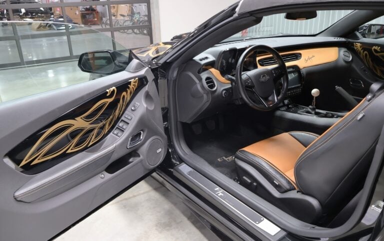 Interior of a sports car with tan and black leather seats, open door, custom dashboard, and steering wheel in a showroom