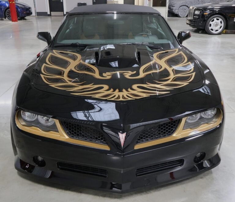 Black Pontiac Firebird with gold flame graphics on hood and headlights, parked in showroom