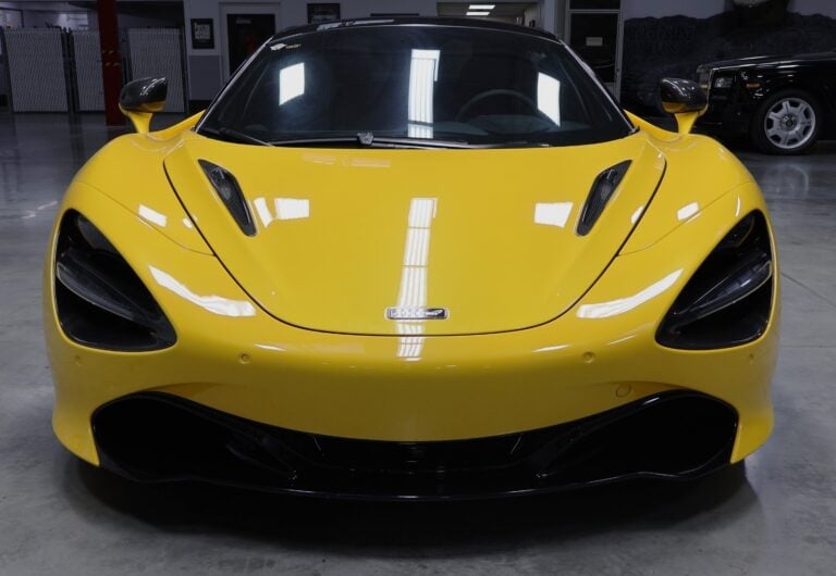 Bright yellow supercar viewed from front in modern showroom with polished concrete floor