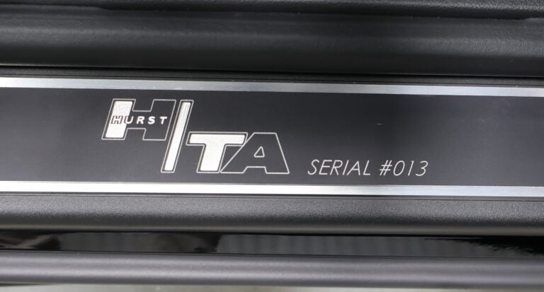 Close-up of Hurst Ita badging on dark gray car panel showing serial number 013