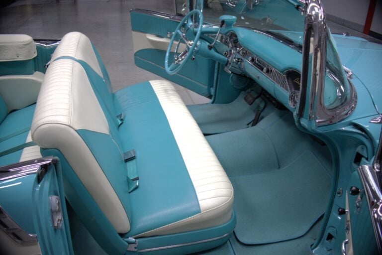 Interior view of a classic turquoise and white convertible car showing the front bench seats and dashboard
