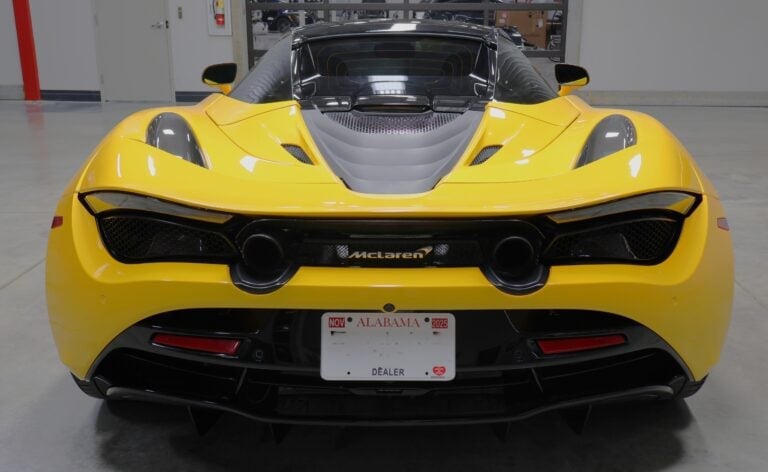Bright yellow McLaren sports car photographed from rear view in a garage, showing sleek aerodynamic design and license plate