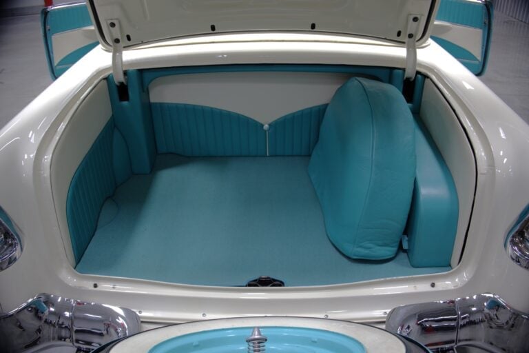 Open trunk of a classic white and turquoise car showing empty interior with turquoise vinyl seats and trim